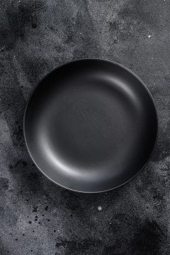 Black plate on textured black background. Top view. Copy space